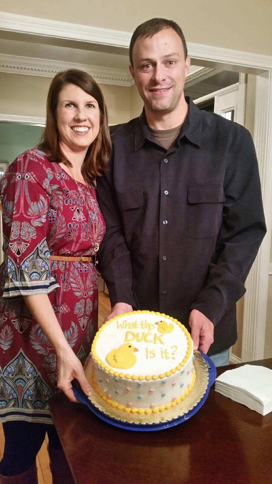 Man and woman stand holding a cake with a duck on it.