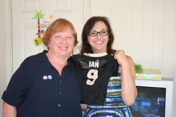two grandmothers stand holding a tiny football jersey with a name on the back