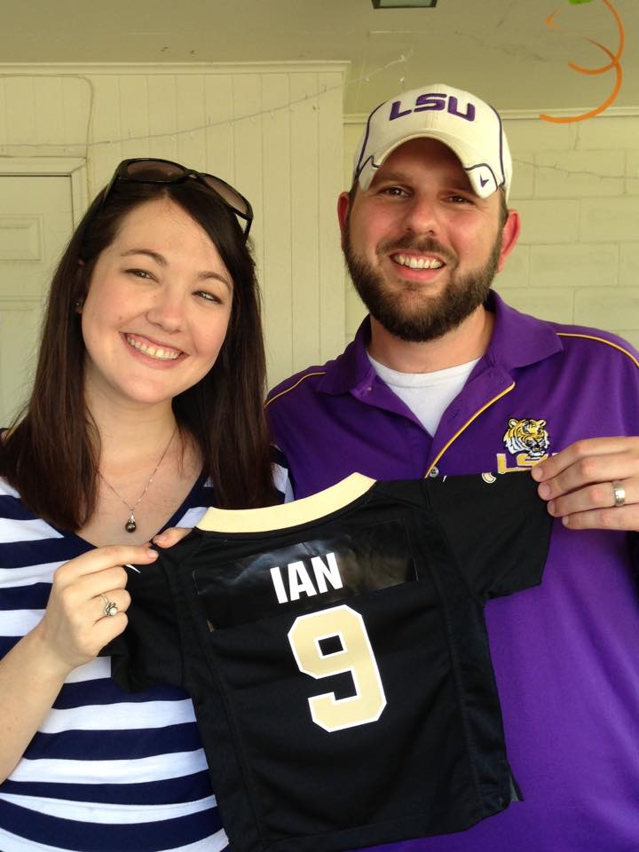 couple stands holding tiny Saints football jersey with name on the back