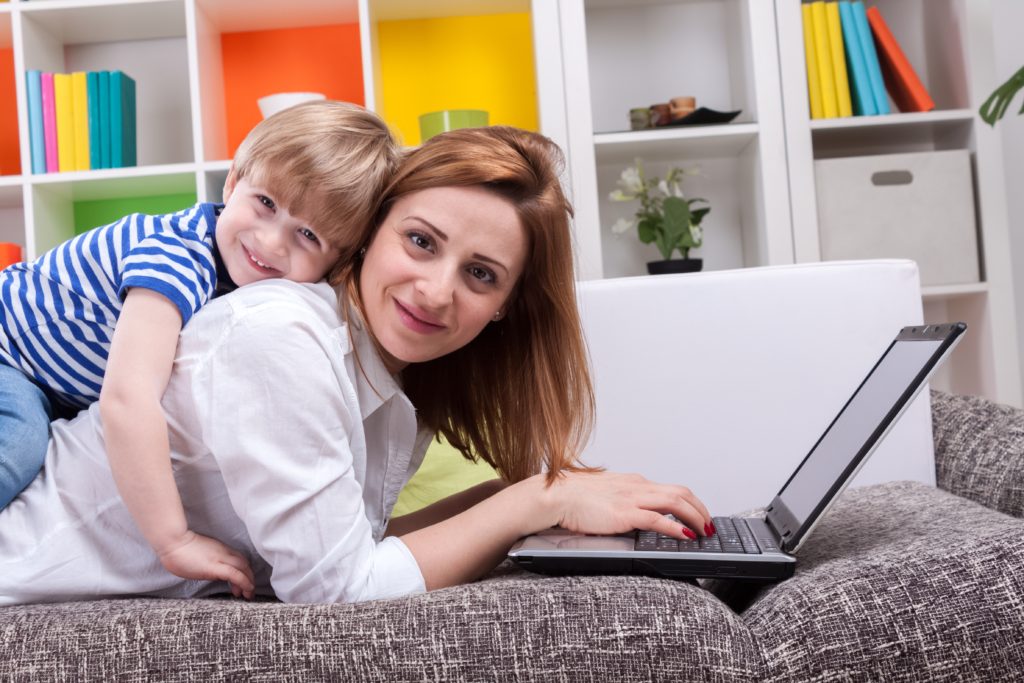 Woman with child lie on sofa and using computer