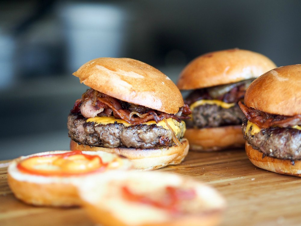 several hamburgers on a wood surface and an open bun 