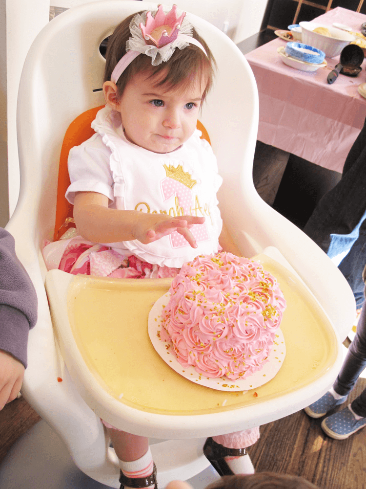 little girl with a pink crown in front fo a pink and gold smash cake.